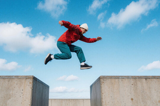 Man performs parkour jump over concrete blocks against blue sky. Athlete shows agility and focus in urban setting. Dynamic motion outdoor activity.