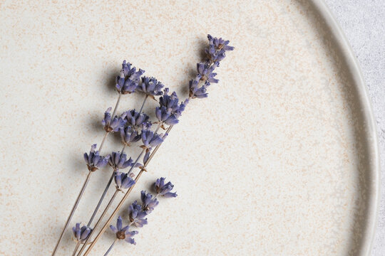 Dried lavender flowers arranged on a textured beige plate, showcasing delicate purple blooms against a neutral background for decorative purposes