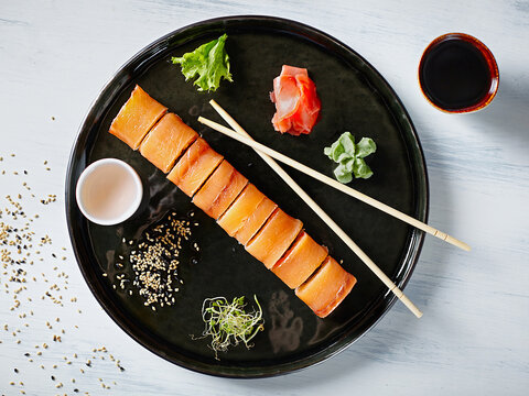 Top view round plate with a serving of Japanese rolls. In round black plate.