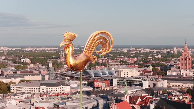 Aerial shot of the iconic golden rooster weather vane atop Saint Peters Church spire standing high above the urban cityscape of Riga, Latvia.