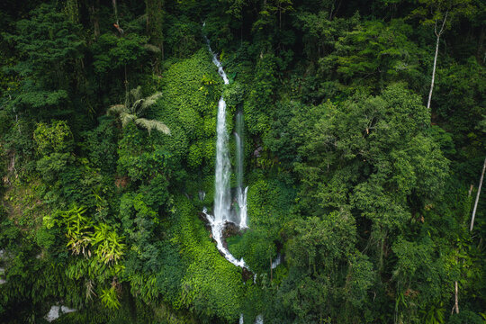 Aerial view of Tiu Kelep Waterfall cascading down through lush tropical rainforest with dense green foliage and rocky terrain in Bayan, West Nusa Tenggara, Indonesia.