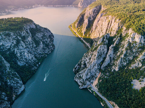 Boat navigating the Danube River through the scenic Iron Gates gorge, surrounded by rugged cliffs and a winding road