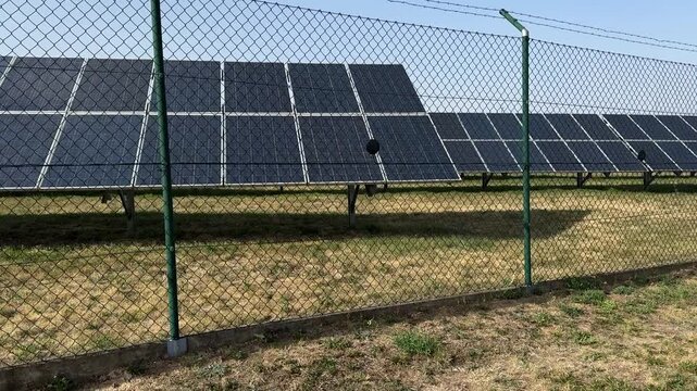 Solar panels stand behind a security fence at a photovoltaic power station producing renewable electricity from sunlight. Solar energy, cleaner power, green technology, sustainable electricity output.