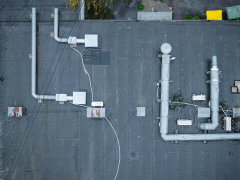 Aerial view of a flat rooftop with metallic ventilation ducts and pipes on a wet surface during a rainy day in Riga, Latvia.