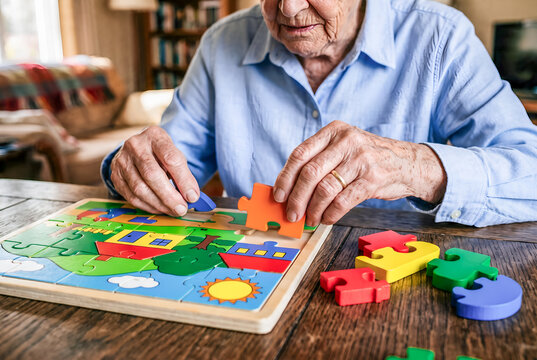 Senior person assembling a colorful jigsaw puzzle at home. representing leisure, cognitive activity, concentration, and active aging.