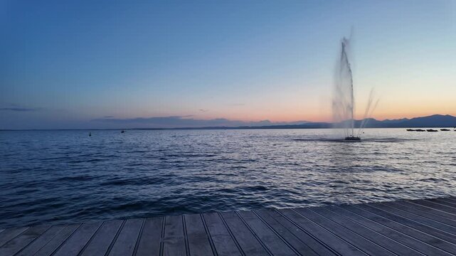 Bardolino, Italy - May 17, 2026 - Serene lake fountain at dusk with wooden pier and distant mountains