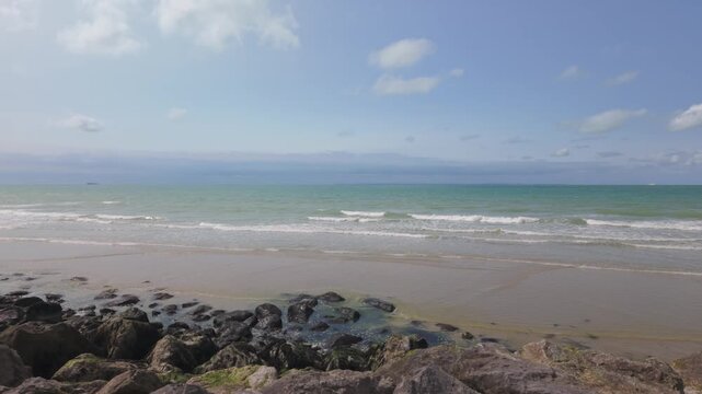 Serene coastal landscape with gentle waves on a rocky beach. Cinematic tracking shot.