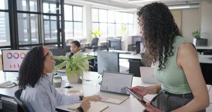 Diverse coworkers at desk while standing woman coming with tablet checking laptop charts