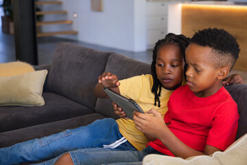 Two African youth males sitting on dark gray sofa wearing yellow and red T-shirts, watching tablet © WavebreakMediaMicro