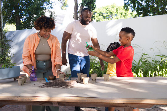 African family planting in pots on backyard patio, parents guiding children using spray bottles