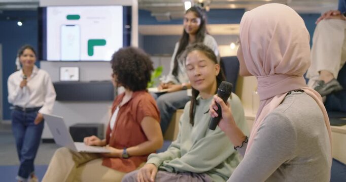 Diverse female panel in meeting area passing microphone after host cue, headscarfed woman speaking