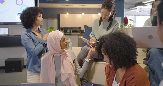 Diverse team watching hijab woman presenting on laptop at office nook taking notes aligning plan
