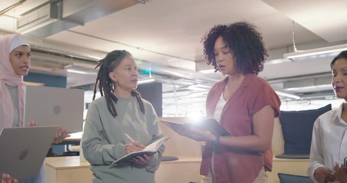 Diverse women coworkers at office, teammates joining, speaker opening notebook and leading stand-up