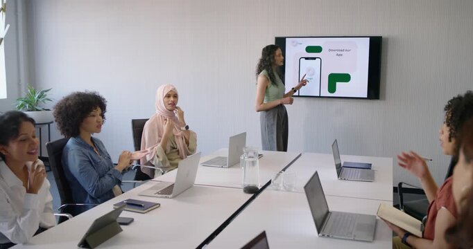 Female presenter in green pointing at screen showing app mockup sparking clapping in meeting room