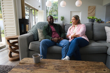 Naklejka premium African American couple sitting and talking on gray sectional sofa in living room with coffee table
