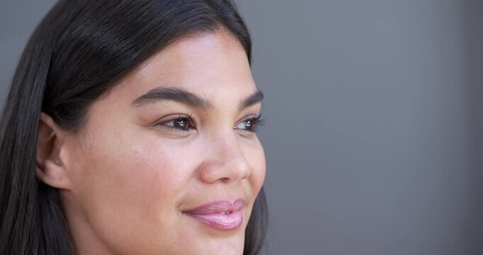 African American woman following off-camera cue, blinking and smiling on grey wall background