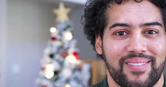 African American man in dark-green top at home smiling, responding to camera at Christmas tree