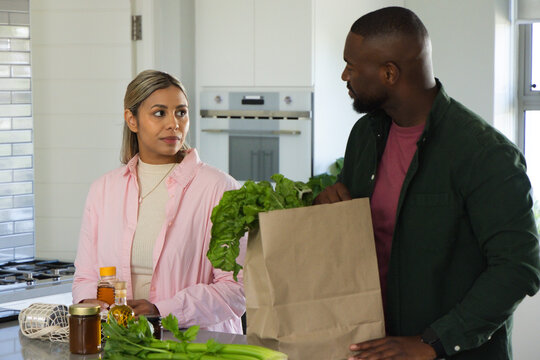 African American couple unpacking at kitchen island, woman in pink shirt holding lettuce