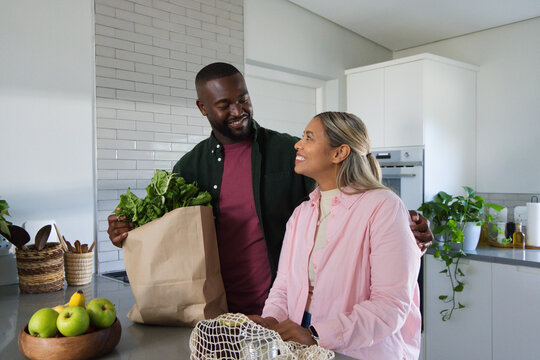 African American couple standing at kitchen island holding brown bag of greens and smiling