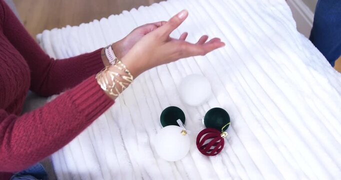 With four loose ornaments, woman's hands are arranging and checking them on blanket to form cluster
