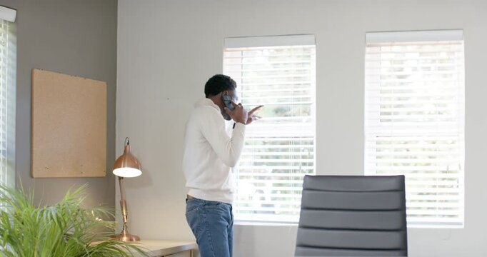 Receiving call, African American man talking on phone for work, pacing by windows, pointing outside