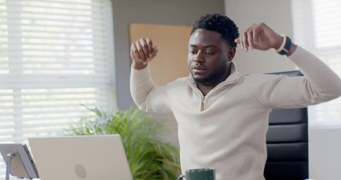 African American man sitting in office stretching after sitting, fiddling bracelet