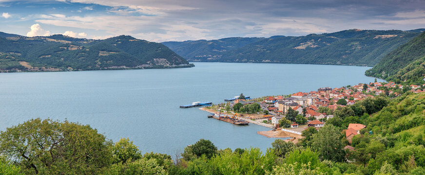 A small riverside town nestled between lush forested hills opens onto a wide calm river, inviting exploration of Europe's hidden waterways. Travel concept.