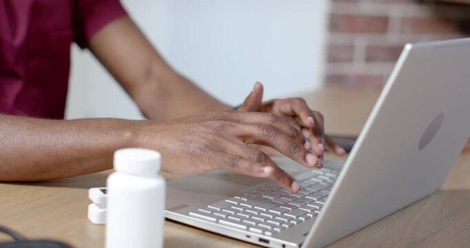 Hands are typing after rest on silver laptop at wooden desk, working with pill case nearby