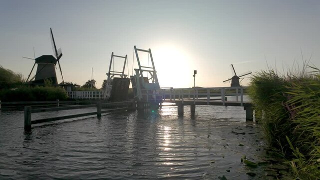 Iconic Dutch windmills and drawbridge at sunset in Kinderdijk, Netherlands. Scenic canal with water reflection.