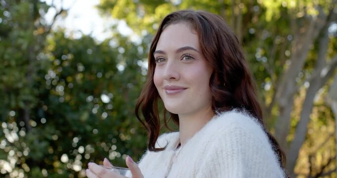 Woman in white knit holding clear cup on porch, noticing offscreen cue, smiling