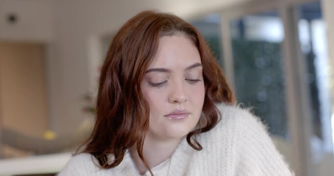 Woman in chunky sweater, nose ring, looking down at table in kitchen, blinking, triggered by object