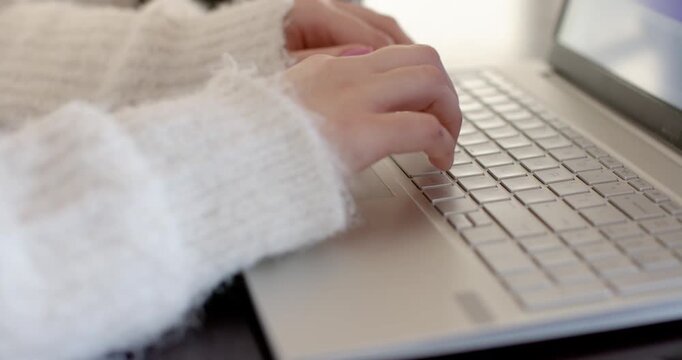 Fingers lightly touching keys are typing on silver laptop at desk, composing message and pausing