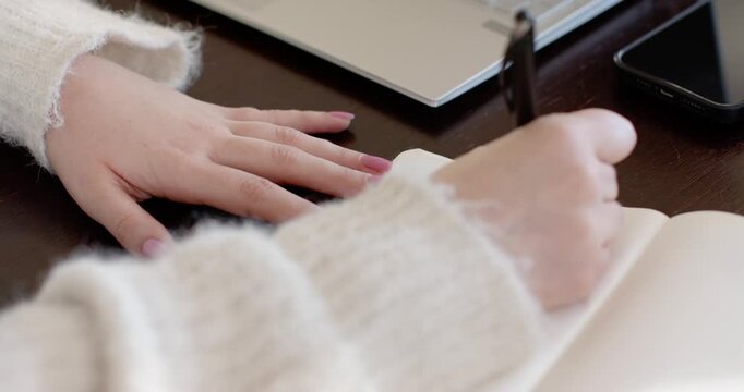 Pen is lowering, right hand is taking notes while left hand is steadying notebook at desk