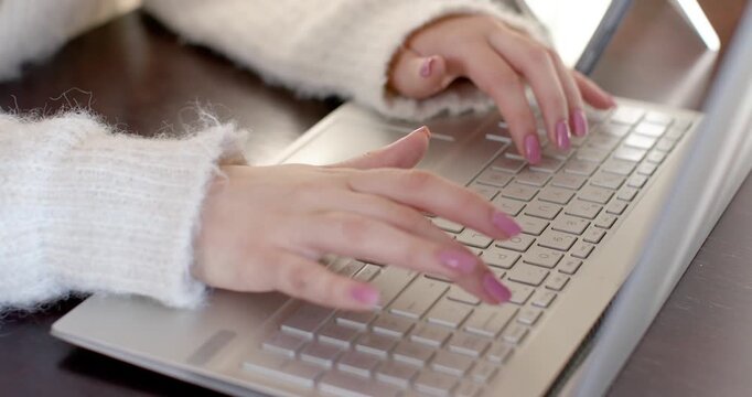 Resting fuzzy-sleeved hands are starting light rhythmic keystrokes on silver laptop, typing work