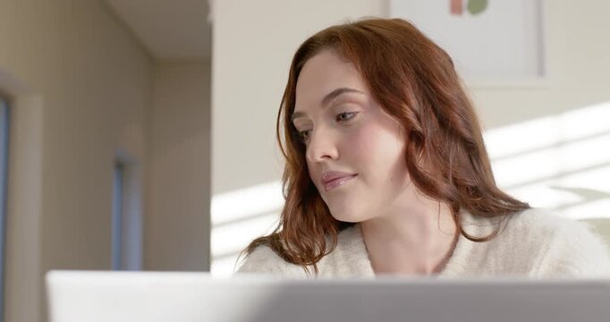 Woman in cream sweater glancing left, turning and lowering gaze, reading on laptop at home