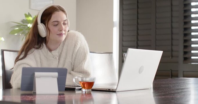 Getting call for meeting, woman 20s wearing headset leaning toward tablet at table