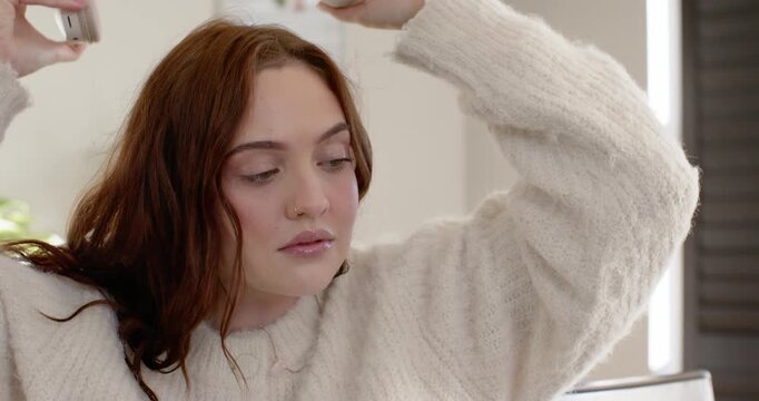 Adult woman in chunky sweater lifting headset beside, adjusting fit and settling to listen at home