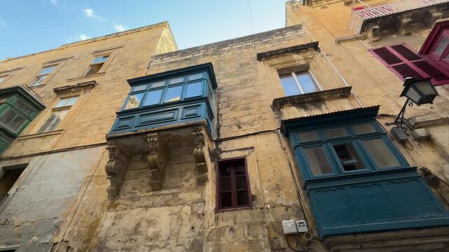 enclosed timber balconies stacked blue maroon green line valletta facade ornate stone corbels shuttered windows upward angle handheld footage malta historic architecture old town craftsmanship