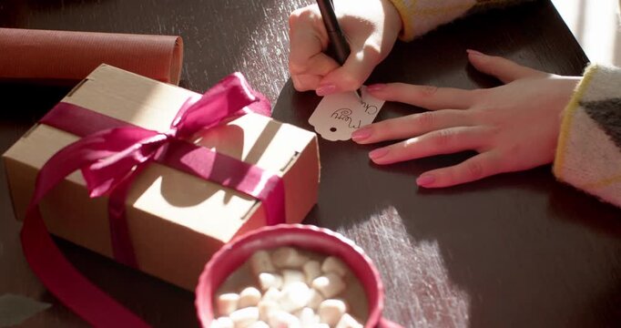 Hands entering from right are placing tag, drawing note and preparing magenta gift on table