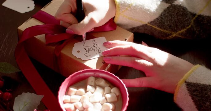 Right hand is touching tag and writing Merry Christmas while left is steadying box on table