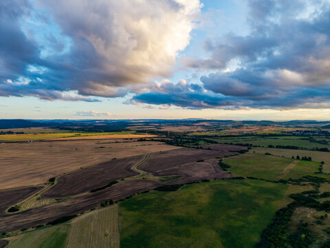 Aerial view of the agricultural landscape near Lezky with rolling fields and dramatic sunset clouds in Lubenec, Usti nad Labem Region, Czechia.