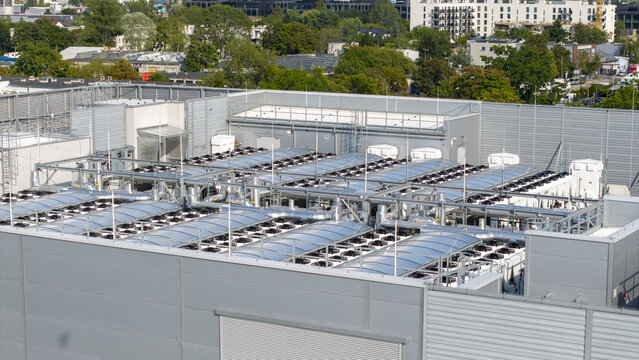 Aerial view of an ai data center rooftop featuring rows of industrial cooling fans and ventilation systems, situated in an urban area in Poland.