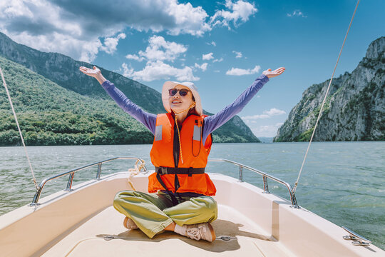 Woman on a boat wearing a life jacket, enjoying a sunny day with arms outstretched, feeling happy and free on water of Danube near Iron Gates gorge