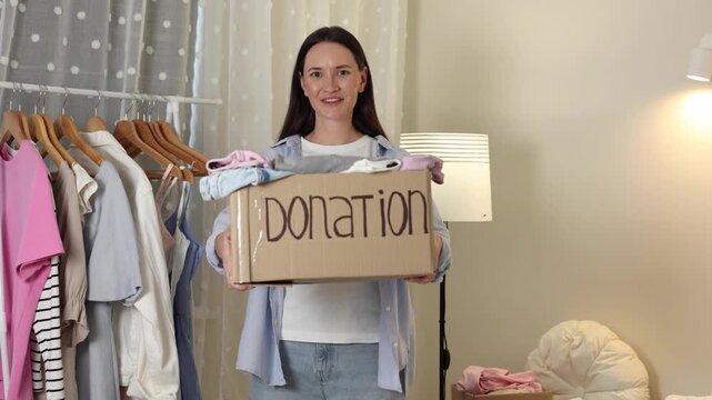 Young woman sorting and donating clothes at home, placing garments into cardboard donation boxes for charity and reuse.