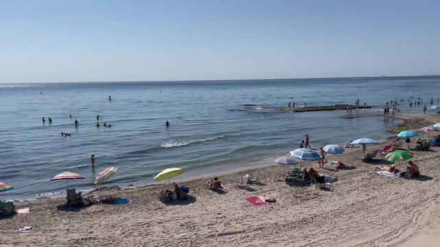 Verano en el mar, sol y playa con ba&ntilde;istas en vacaciones de verano y cielo azul con horizonte 