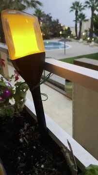 Farol luz artificial efecto llama c&aacute;lida y farolillo de fuego l&aacute;mpara decorativa e iluminaci&oacute;n en terraza con piscina, plantas y flores
