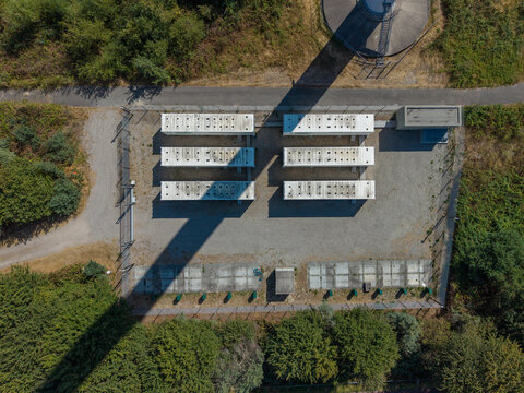 Aerial view of industrial utility site with six white containers arranged in rows, surrounded by trees and gravel, Netherlands.