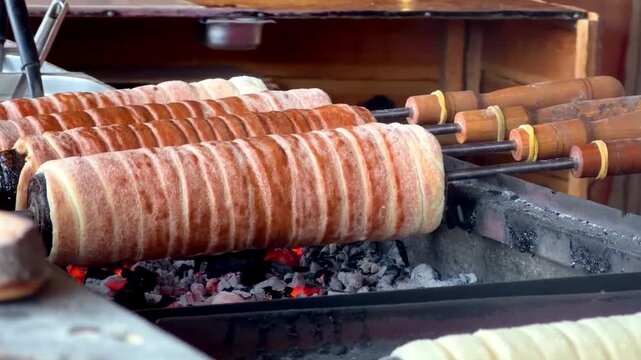 Traditional Chimney Cakes (Kurtoskalacs) Roasting on Spits Over Glowing Charcoal at a Food Market.