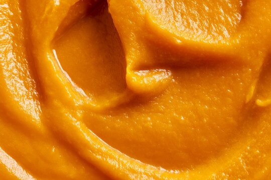 Creamy orange food mixture in a bowl is being prepared for a dish in a kitchen setting during daylight hours