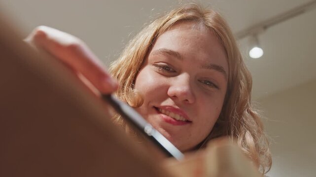 Close up of young woman applying makeup with soft lighting in indoor setting. scene shows her hand holding and using various cosmetic tools on face focusing on precise application techniques